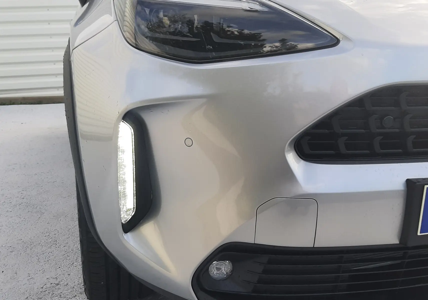 Gros plan sur l'avant gauche d'une Toyota Yaris Cross 130H Design gris minéral avec feux LED et calandre noire.