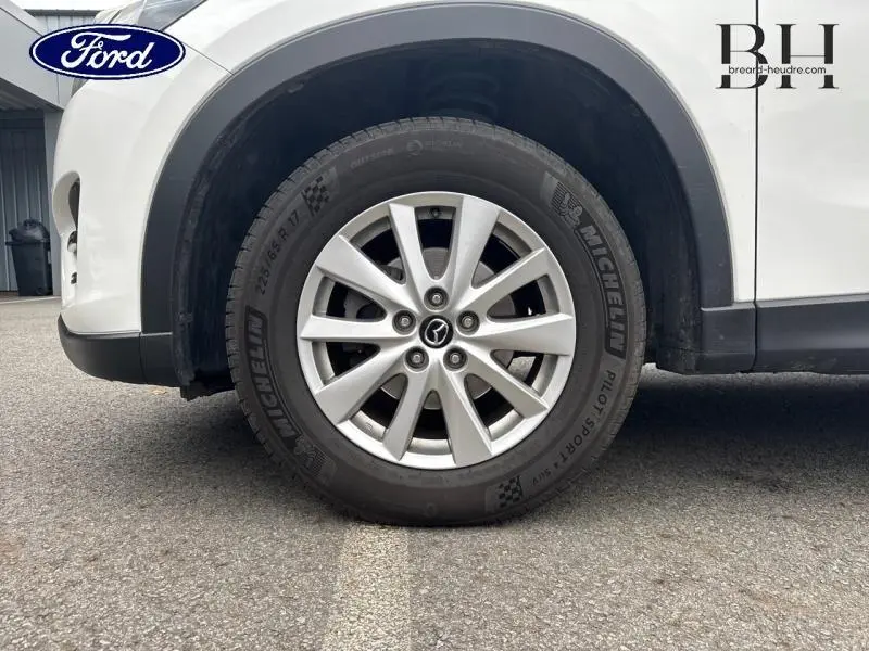 Gros plan sur la roue avant gauche d'un Mazda CX-5 blanc nacré avec jante alliage et pneu Michelin Pilot Sport.