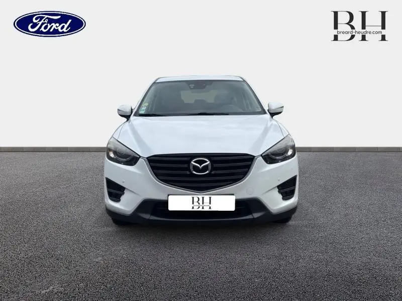 Vue frontale d'un Mazda CX-5 blanc nacré avec calandre noire et phares effilés sur fond neutre.