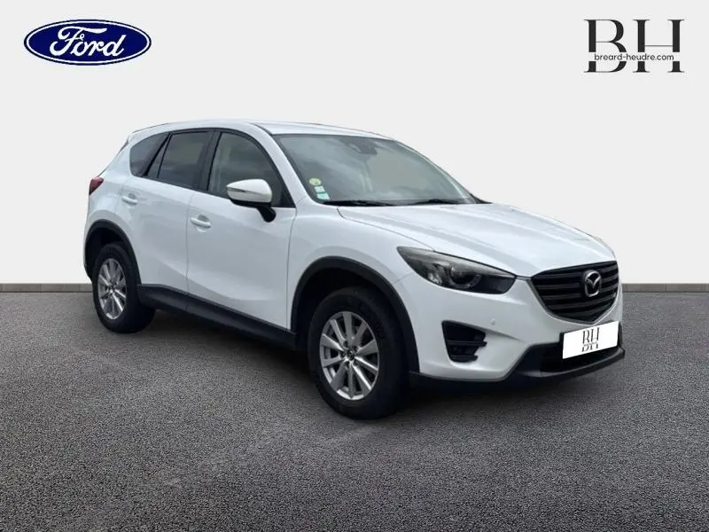 Vue 3/4 avant gauche d'un Mazda CX-5 blanc nacré avec calandre noire et jantes alliage sur fond neutre.