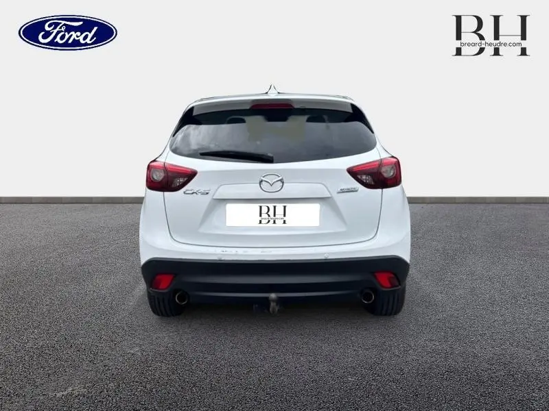 Vue arrière d'un Mazda CX-5 blanc perle avec feux rouges et attelage visible sur un sol gris.