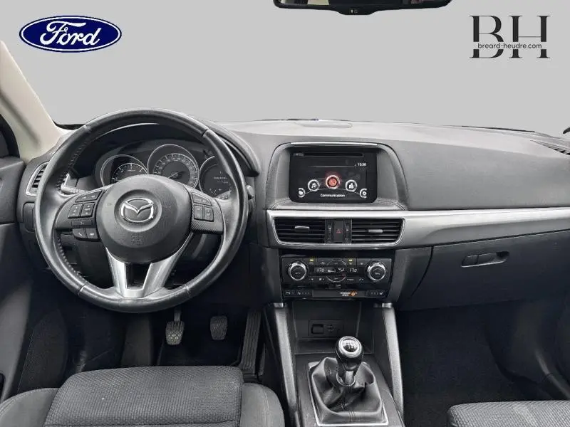 Intérieur avant du Mazda CX-5 2016 avec tableau de bord noir, volant multifonction et levier de vitesse manuel.