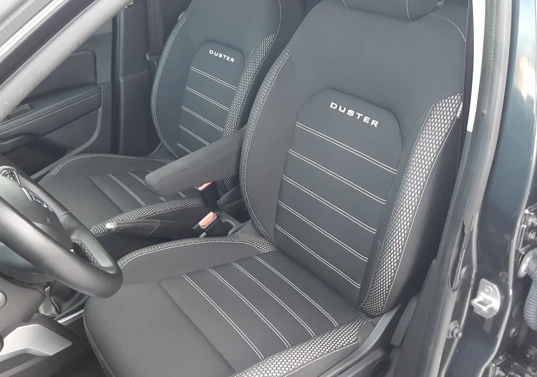 Vue intérieure côté conducteur du Dacia Duster gris Cassiopée 2019, sièges noirs avec logo Duster brodé.