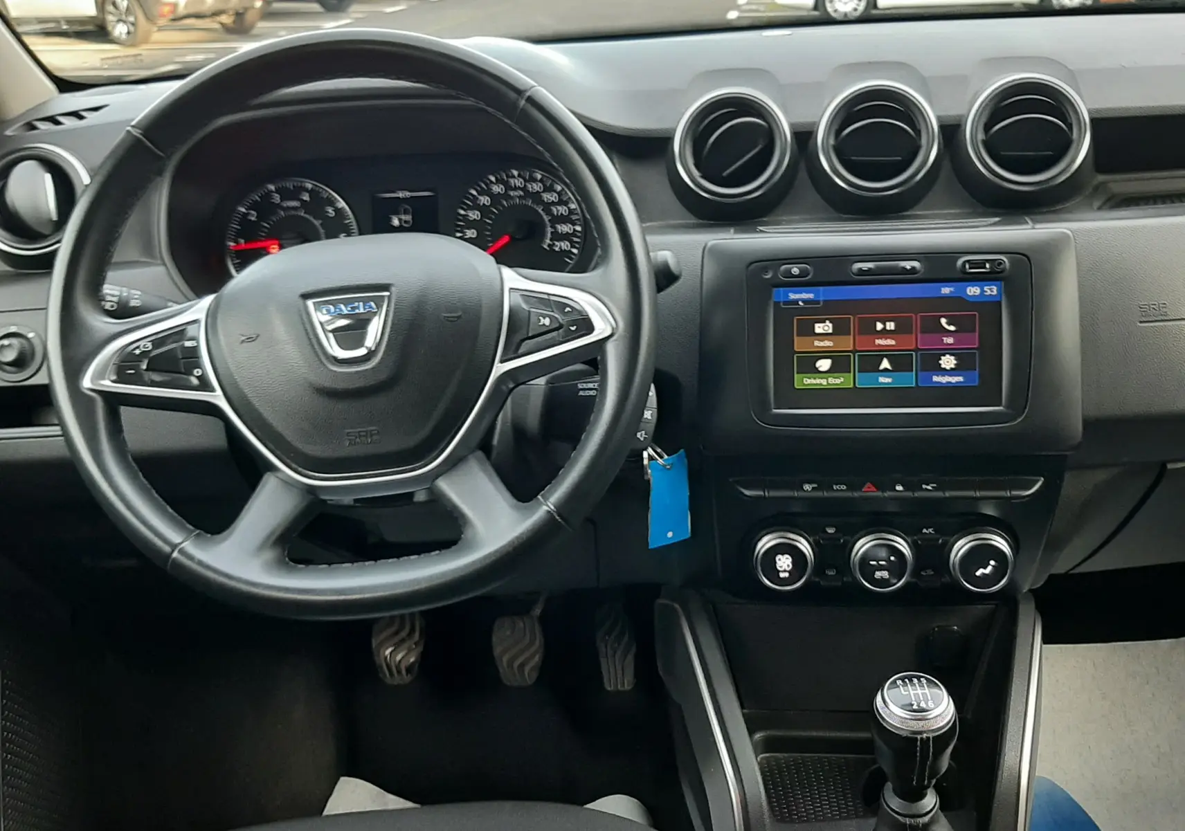 Vue intérieure du tableau de bord du Dacia Duster 2019, volant, écran tactile et levier de vitesse manuelle visibles.
