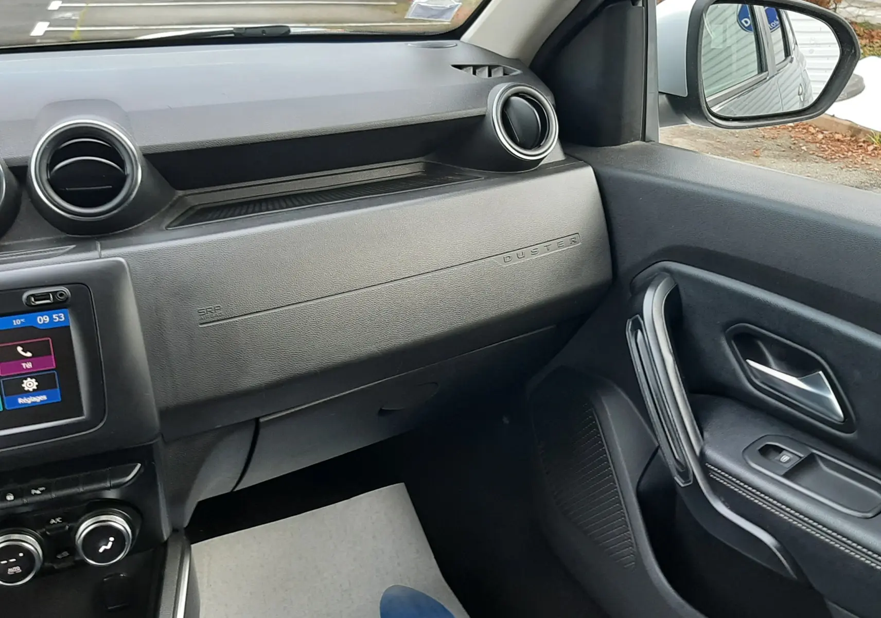 Vue intérieure côté passager du Dacia Duster gris Cassiopée 2019, montrant tableau de bord et portière noire.