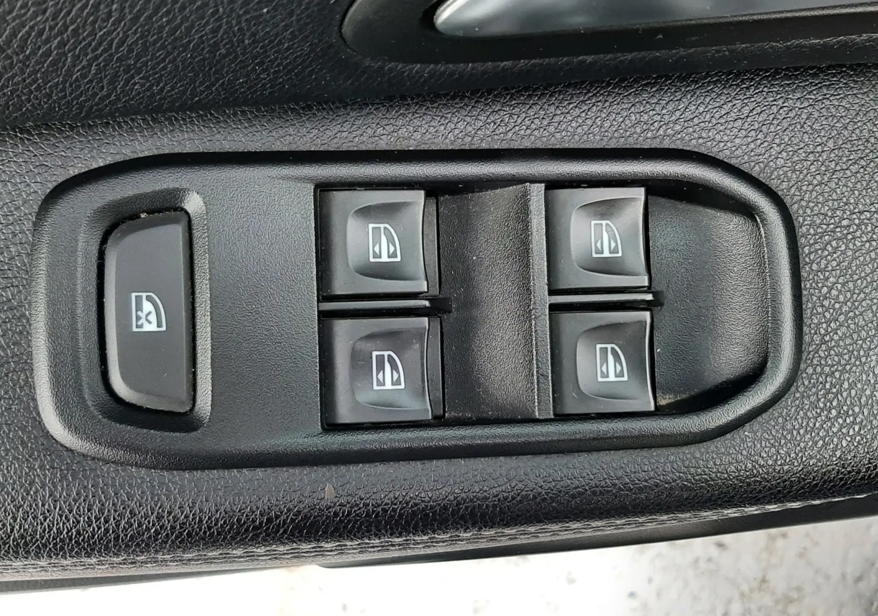 Gros plan sur les commandes électriques des vitres et verrouillage enfant sur la porte intérieure noire du Dacia Duster gris.