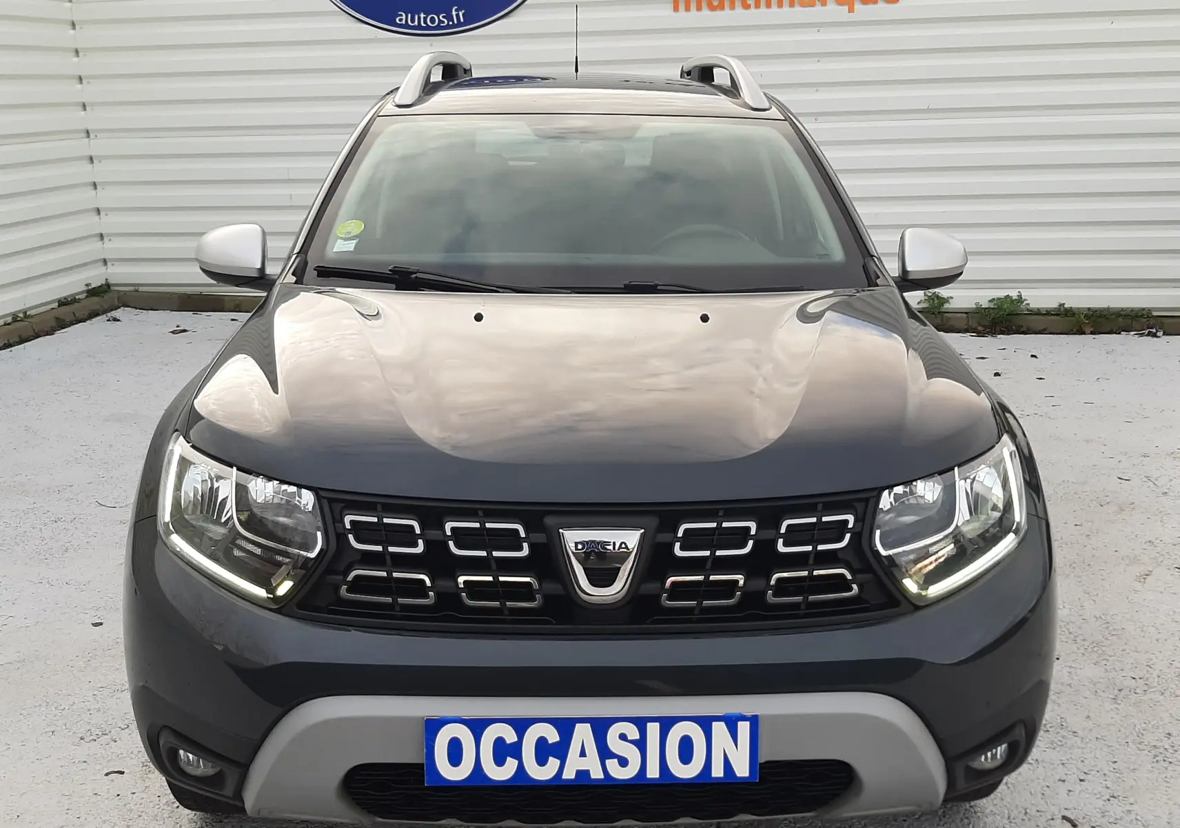 Vue frontale d'un Dacia Duster gris Cassiopée 2019 avec calandre noire et plaque "OCCASION" visible.