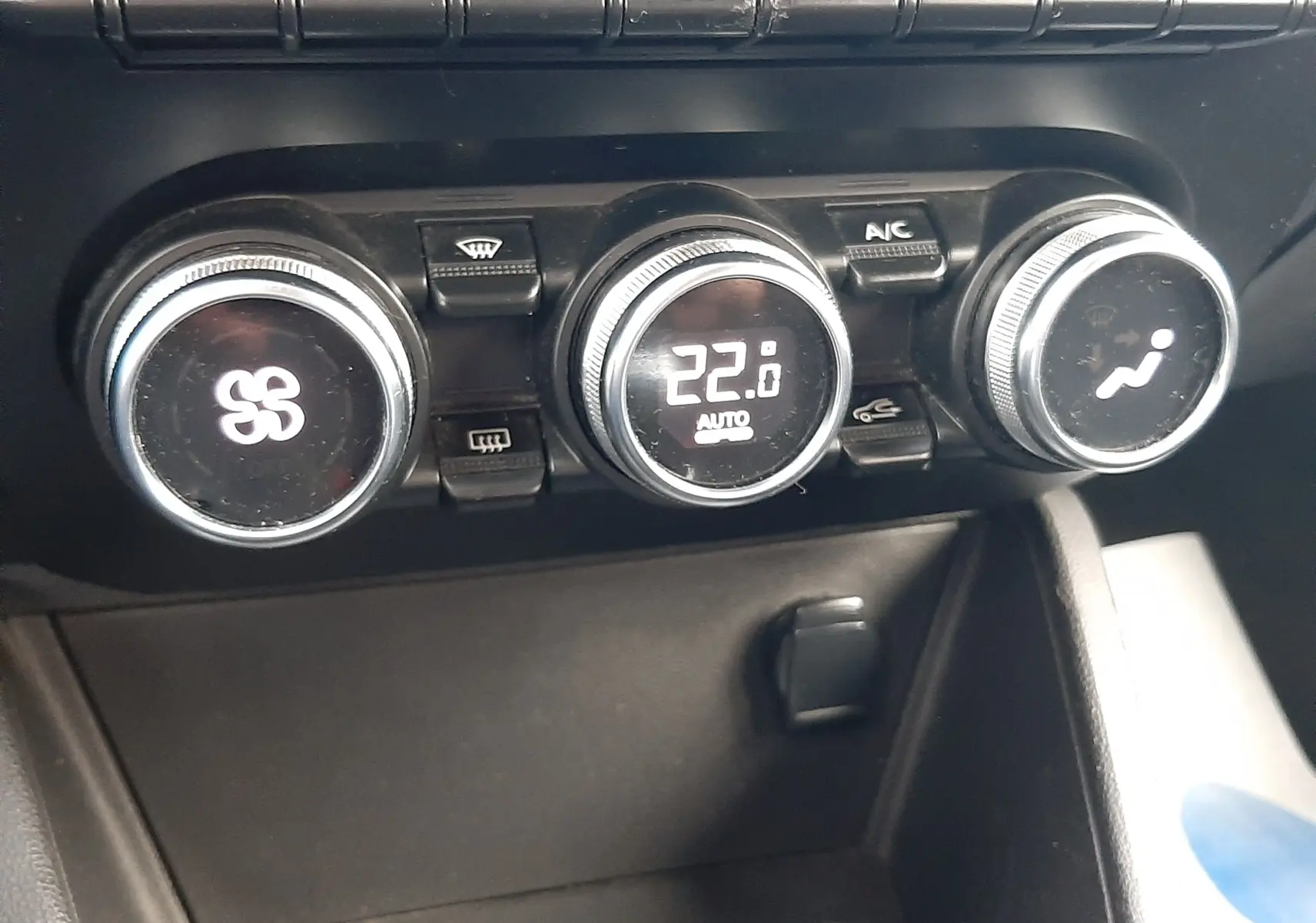 Gros plan sur les commandes de climatisation du Dacia Duster gris Cassiopée, avec boutons rotatifs et touches fonctionnelles.