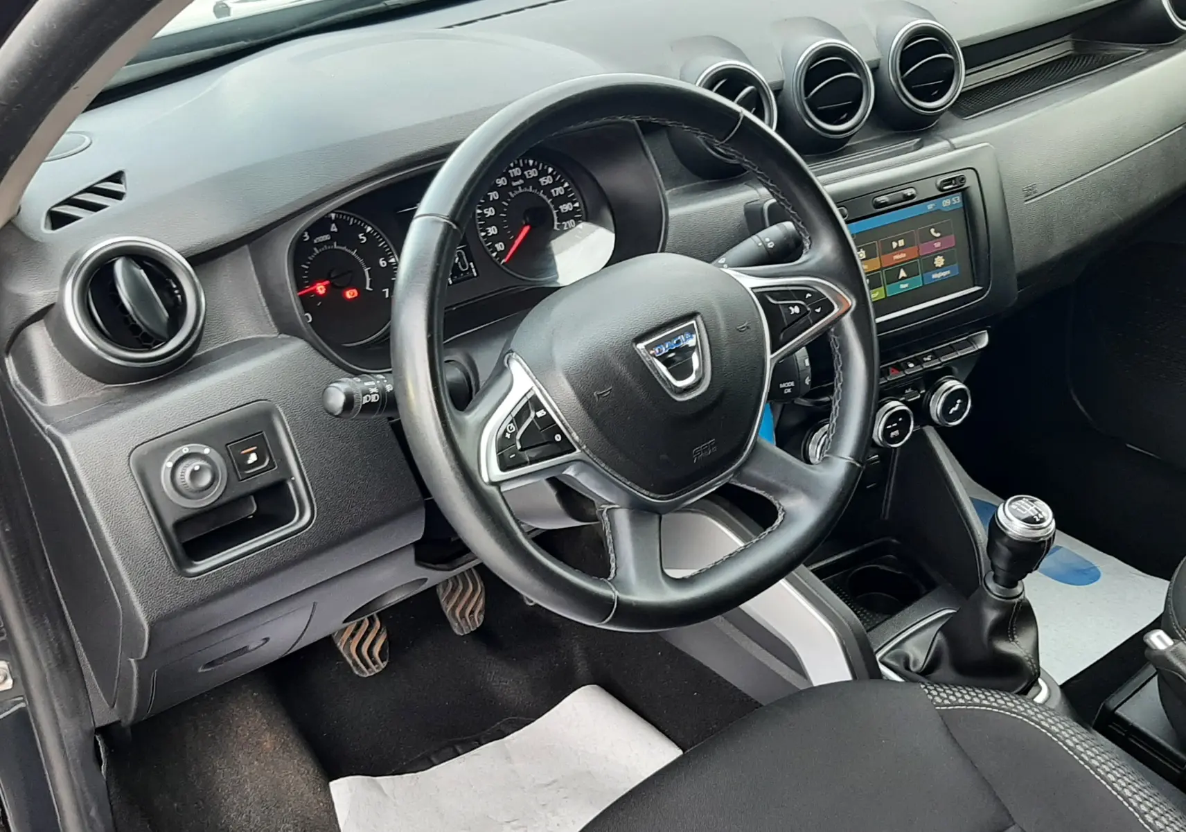 Vue intérieure côté conducteur du Dacia Duster 2019, tableau de bord noir avec volant multifonction et boîte manuelle.