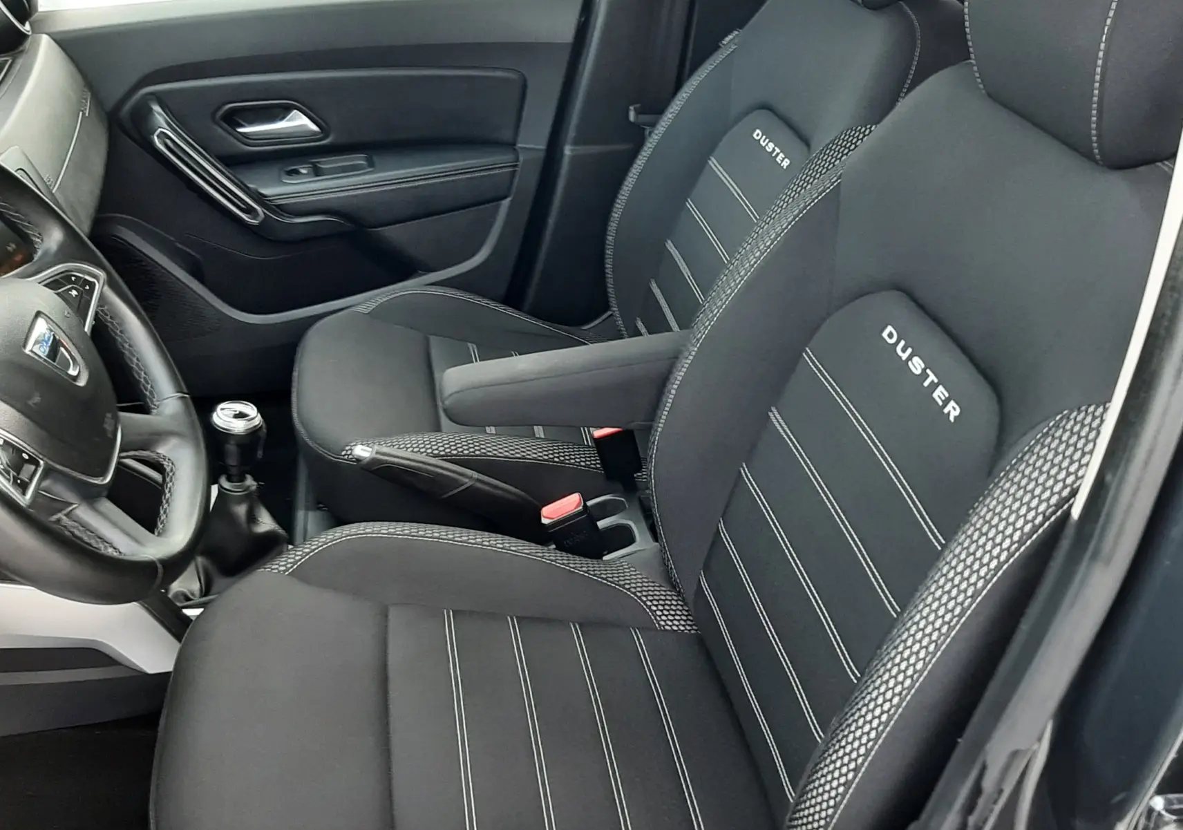 Vue intérieure côté conducteur du Dacia Duster 2019, sièges noirs avec logo DUSTER brodé et coutures contrastées.