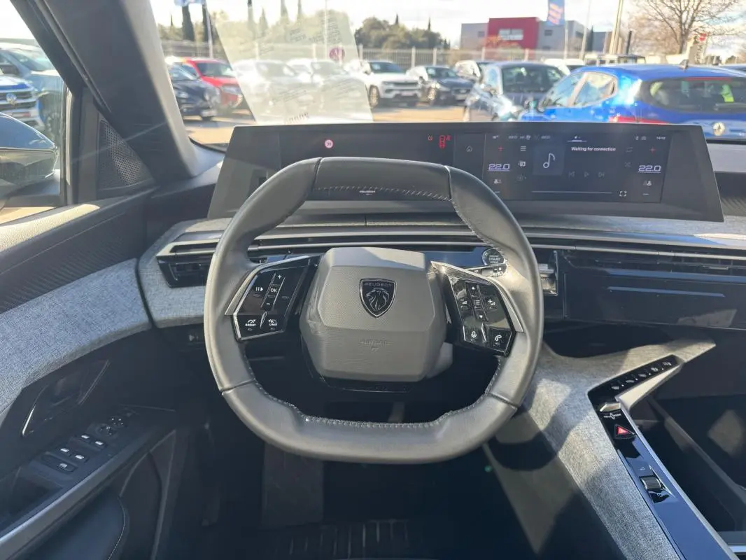 Vue intérieure centrée sur le volant cuir du Peugeot 5008 gris 2025 avec tableau de bord numérique et console moderne.