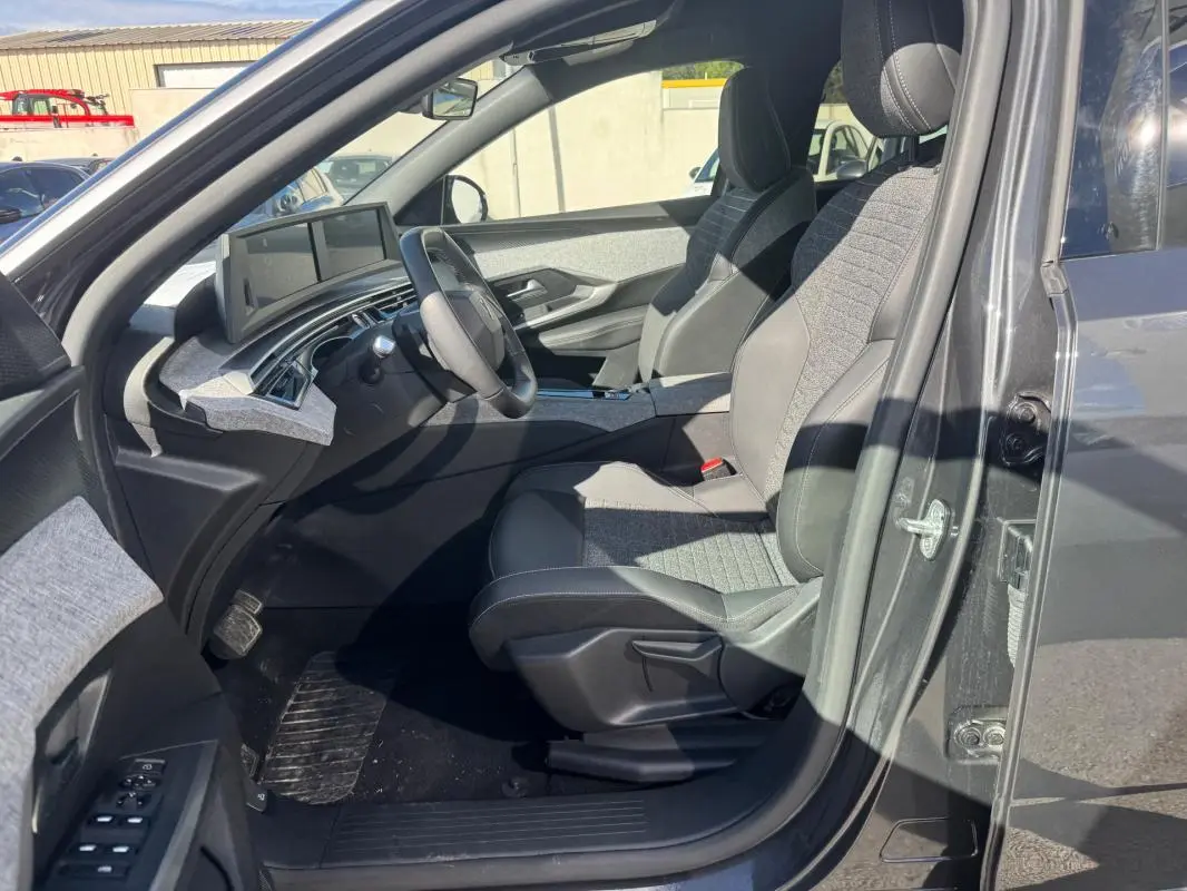 Vue intérieure côté conducteur du Peugeot 5008 Hybrid gris 2025, sièges tissu et cuir, tableau de bord numérique.