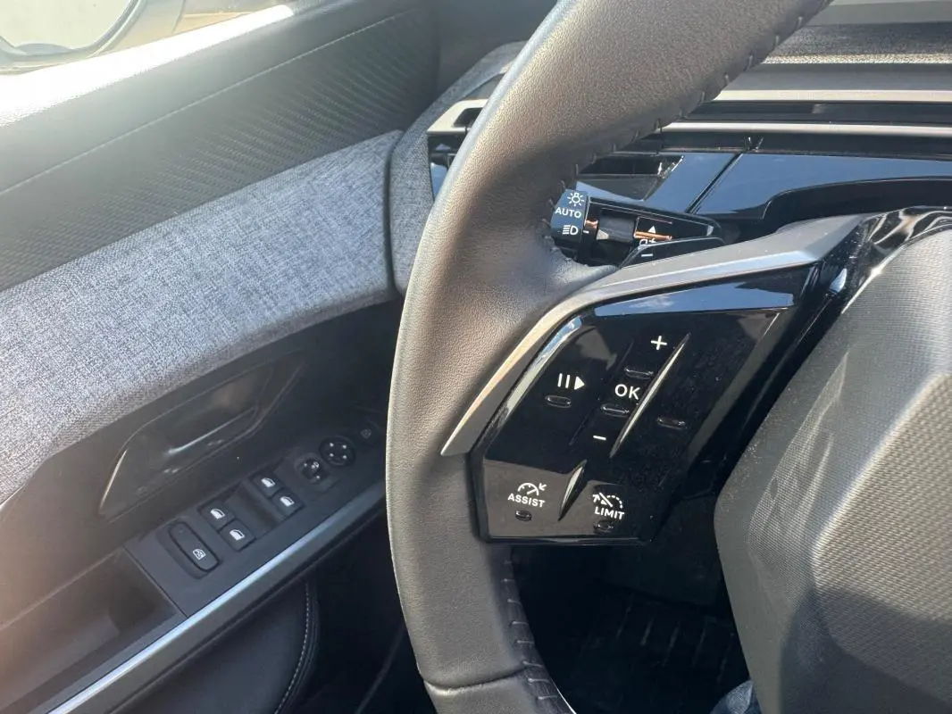 Gros plan sur le volant et la portière côté gauche du Peugeot 5008 gris, avec commandes au volant et boutons de vitres visibles.