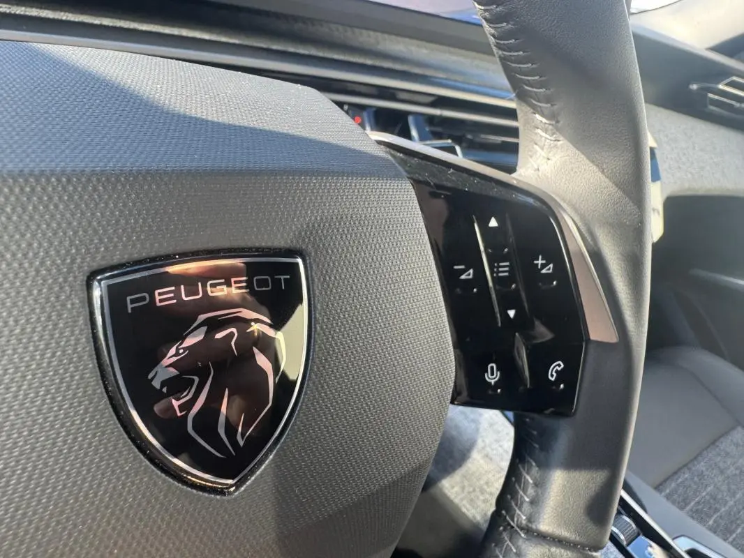 Gros plan sur le volant noir du Peugeot 5008 Hybrid 145 Allure avec logo lion et commandes tactiles à droite.