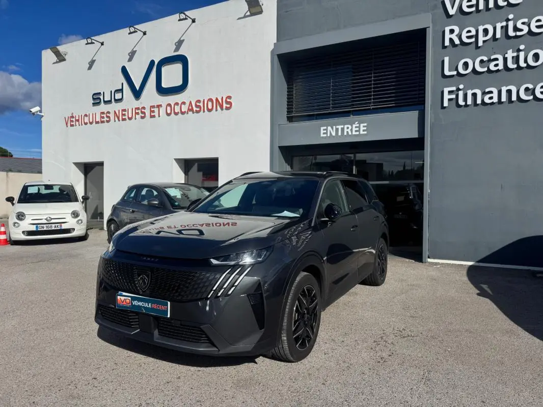 Peugeot 5008 Hybrid gris en 3/4 avant droit, avec jantes alliage noires de 19 pouces, devant un showroom.