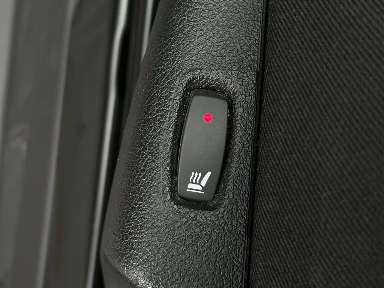 Bouton de siège chauffant avec témoin rouge sur panneau intérieur noir d’un Nissan Primastar noir métal.