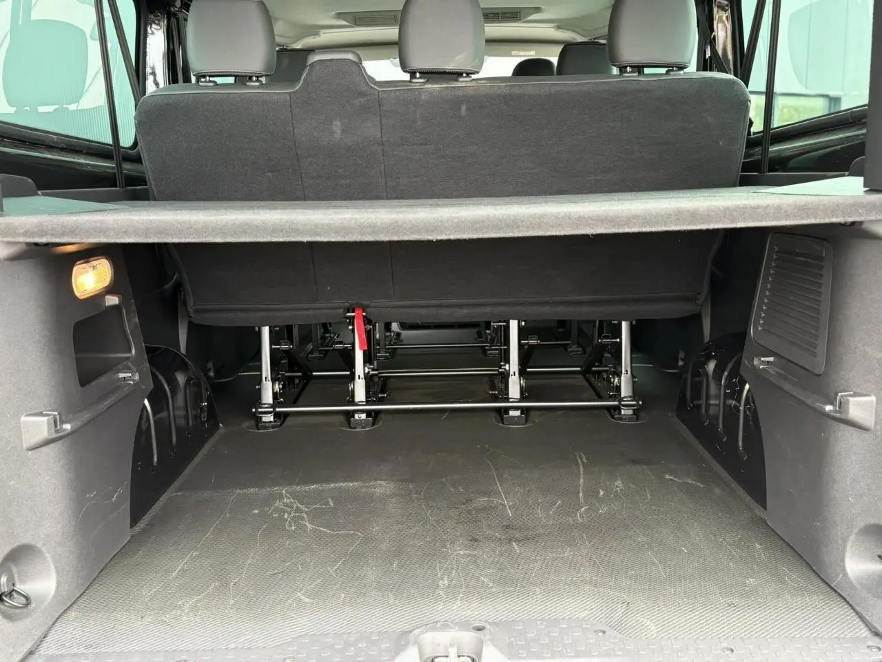 Vue arrière du coffre spacieux du Nissan Primastar noir métallisé avec banquette arrière et cache-bagages visible.
