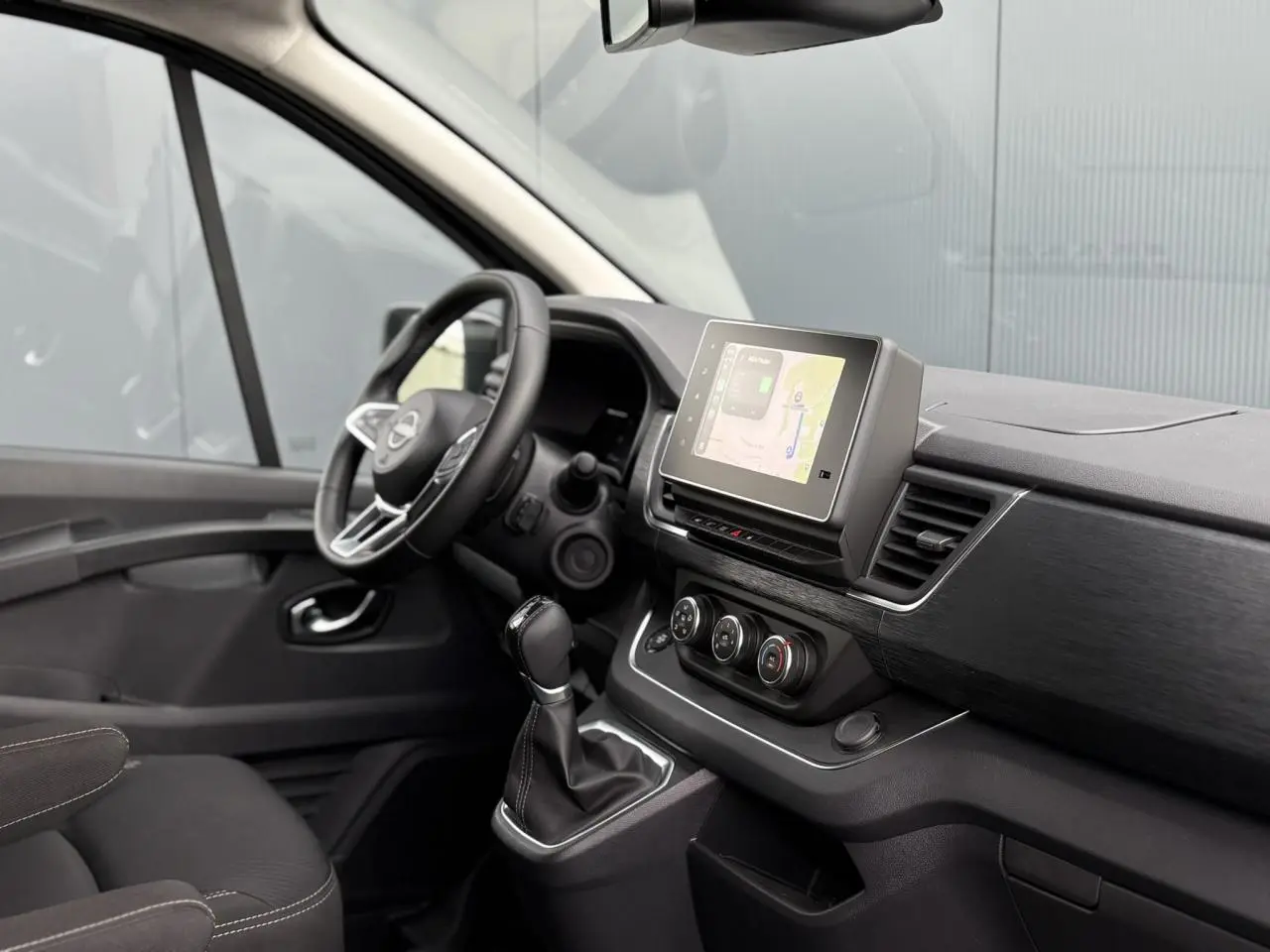 Vue intérieure côté conducteur du Nissan Primastar 2025, tableau de bord noir avec écran tactile et volant multifonctions.
