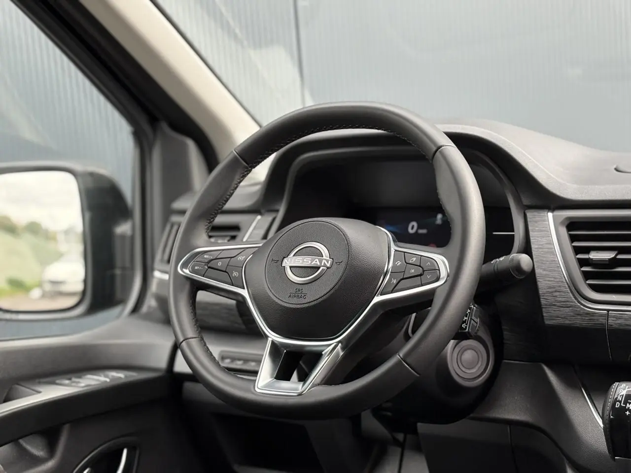 Vue intérieure centrée sur le volant Nissan noir avec commandes intégrées et tableau de bord moderne du Primastar 2025.