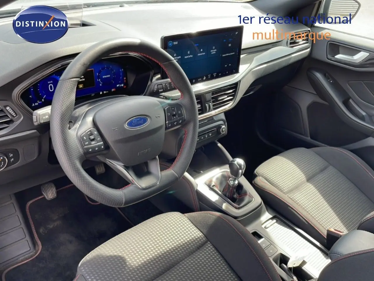 Vue intérieure de la Ford Focus SW 2023, tableau de bord et volant multifonction avec sellerie tissu gris et surpiqûres rouges.