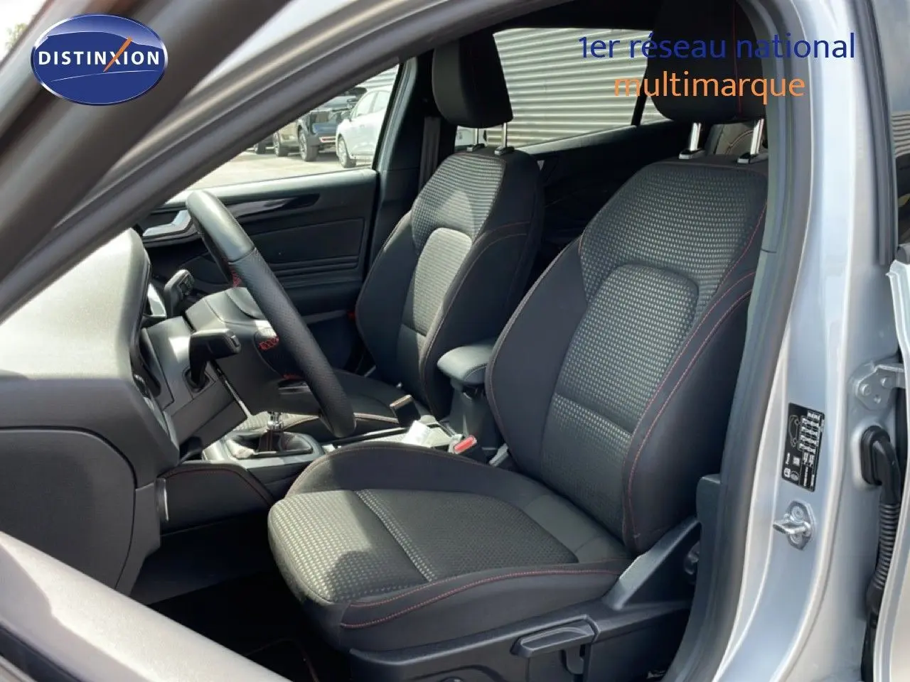 Vue intérieure côté conducteur de la Ford Focus SW gris lunaire, sièges tissu noir avec surpiqûres rouges et volant cuir.