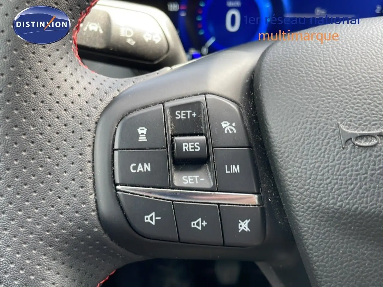 Gros plan sur les commandes noires du volant perforé avec surpiqûres rouges d’une Ford Focus SW gris lunaire 2023.