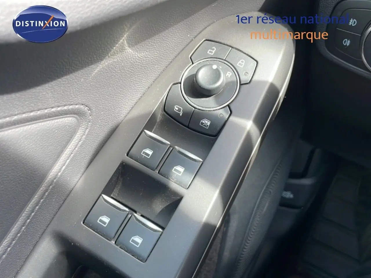 Gros plan sur les commandes de lève-vitres et rétroviseurs côté conducteur d’une Ford Focus SW 2023, intérieur noir.