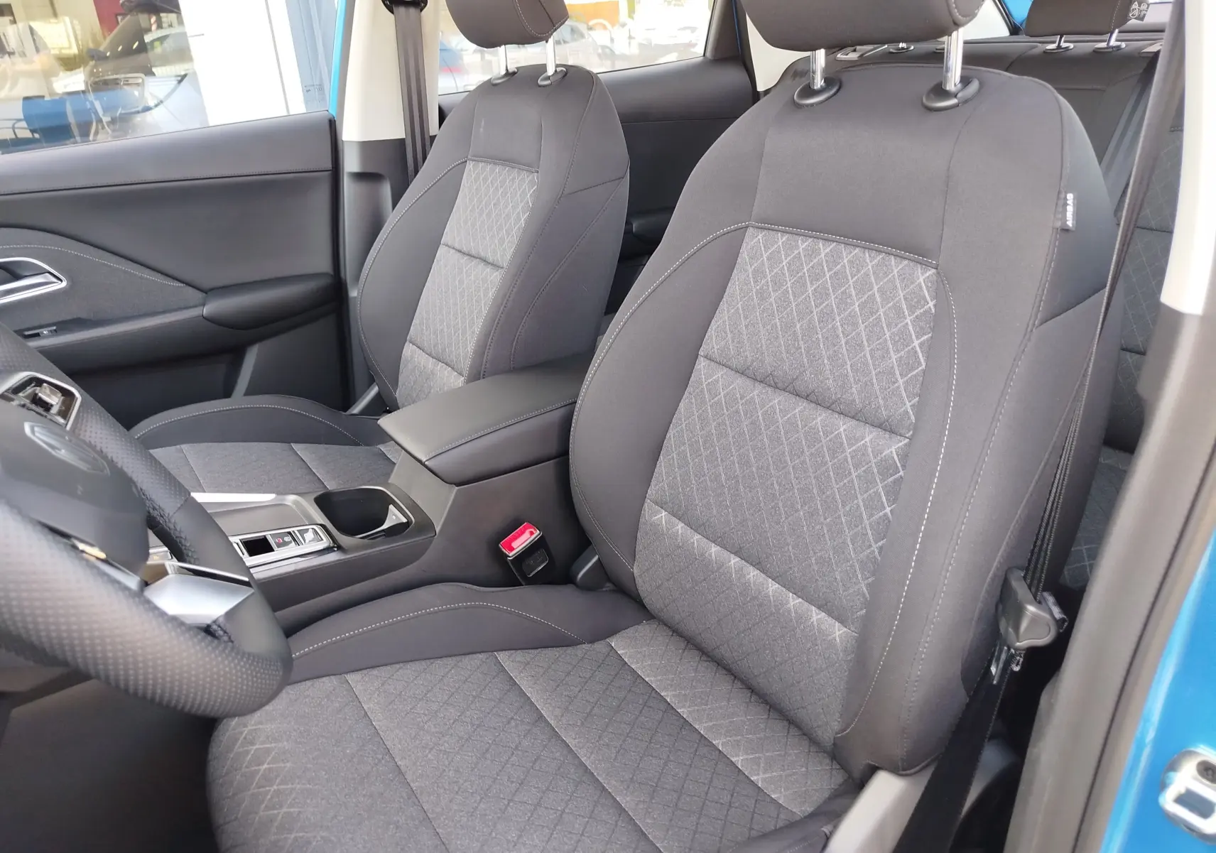 Vue intérieure côté avant droit du MG ZS 2026 avec sièges en tissu noir et accoudoir central, portière Cosmo Blue ouverte.