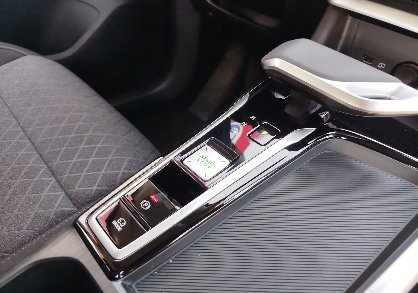 Gros plan sur la console centrale noire brillante du MG ZS 1.5 L Hybrid+ avec levier de vitesse automatique et bouton start/stop.