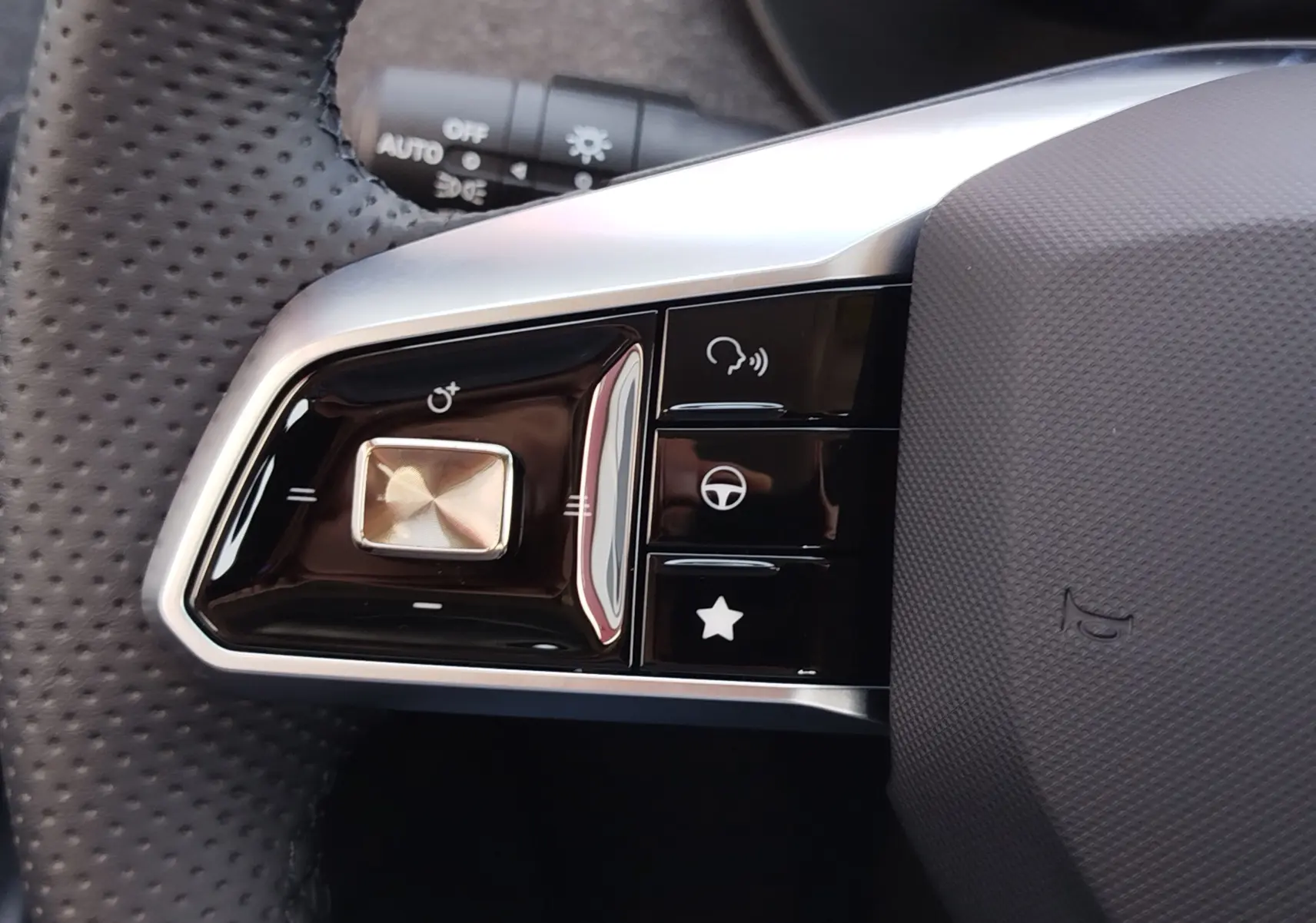 Gros plan sur les commandes gauche du volant noir perforé du MG ZS 1.5 L Hybrid+ 2026 avec finitions argentées.