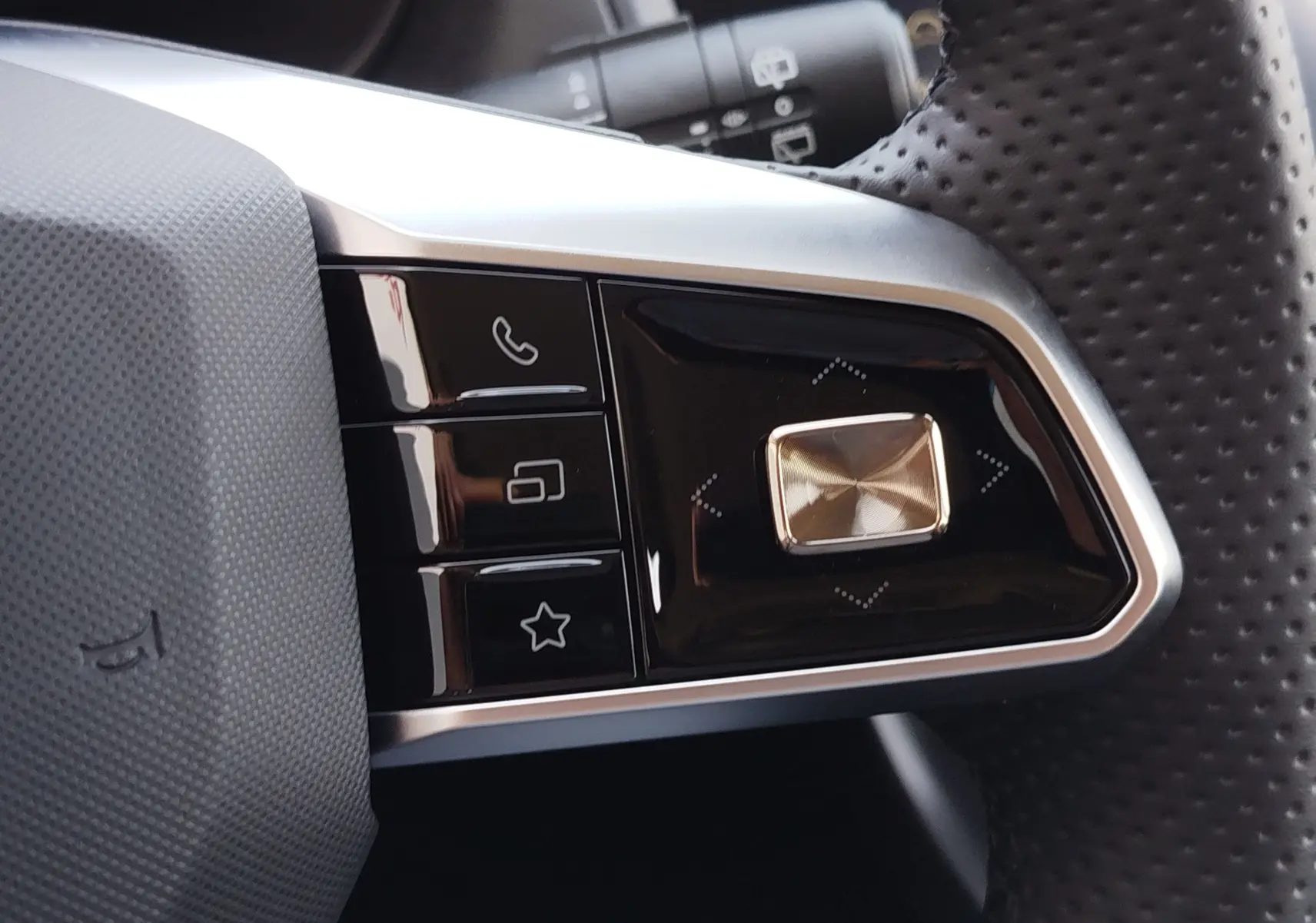 Gros plan sur les commandes gauche du volant perforé du MG ZS 1.5 L Hybrid+ 2026 en Cosmo Blue, boutons noirs et argentés.