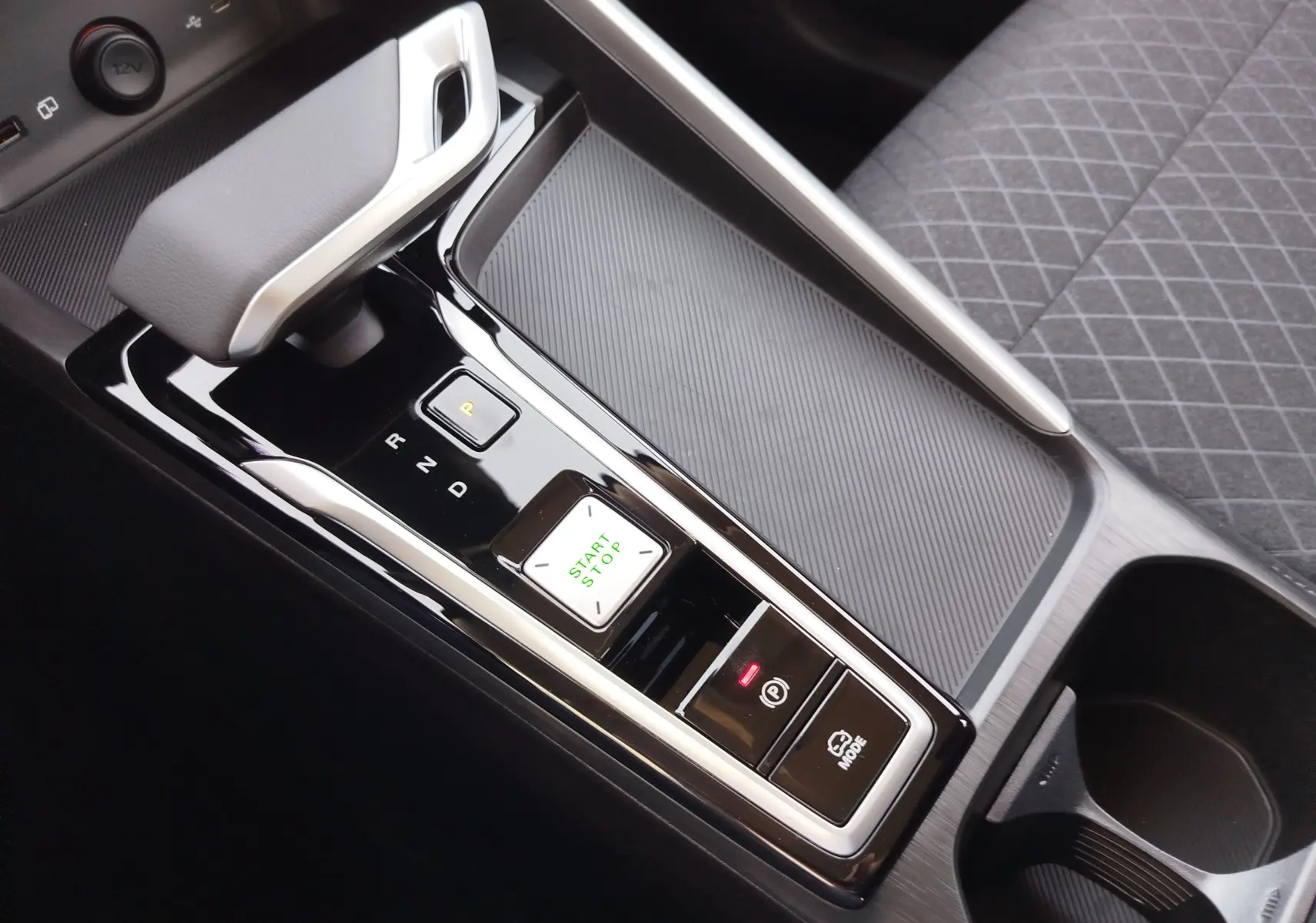 Gros plan sur la console centrale noire brillante du MG ZS 1.5 L Hybrid+ 2026, avec levier de vitesse automatique et bouton start/stop.