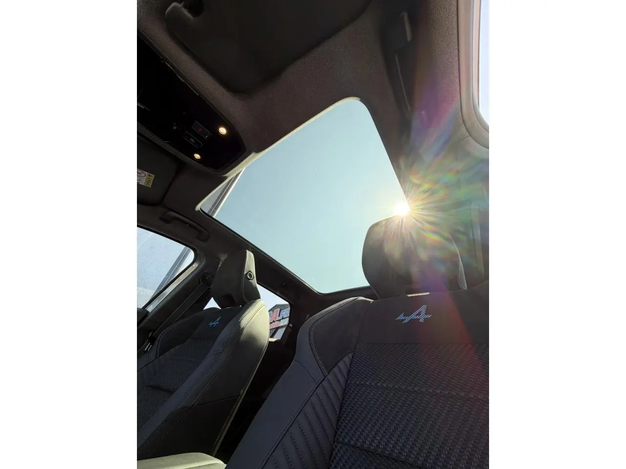 Vue intérieure en contre-plongée du toit panoramique et des sièges avant noirs avec logo Alpine brodé sur Renault Austral E-Tech.