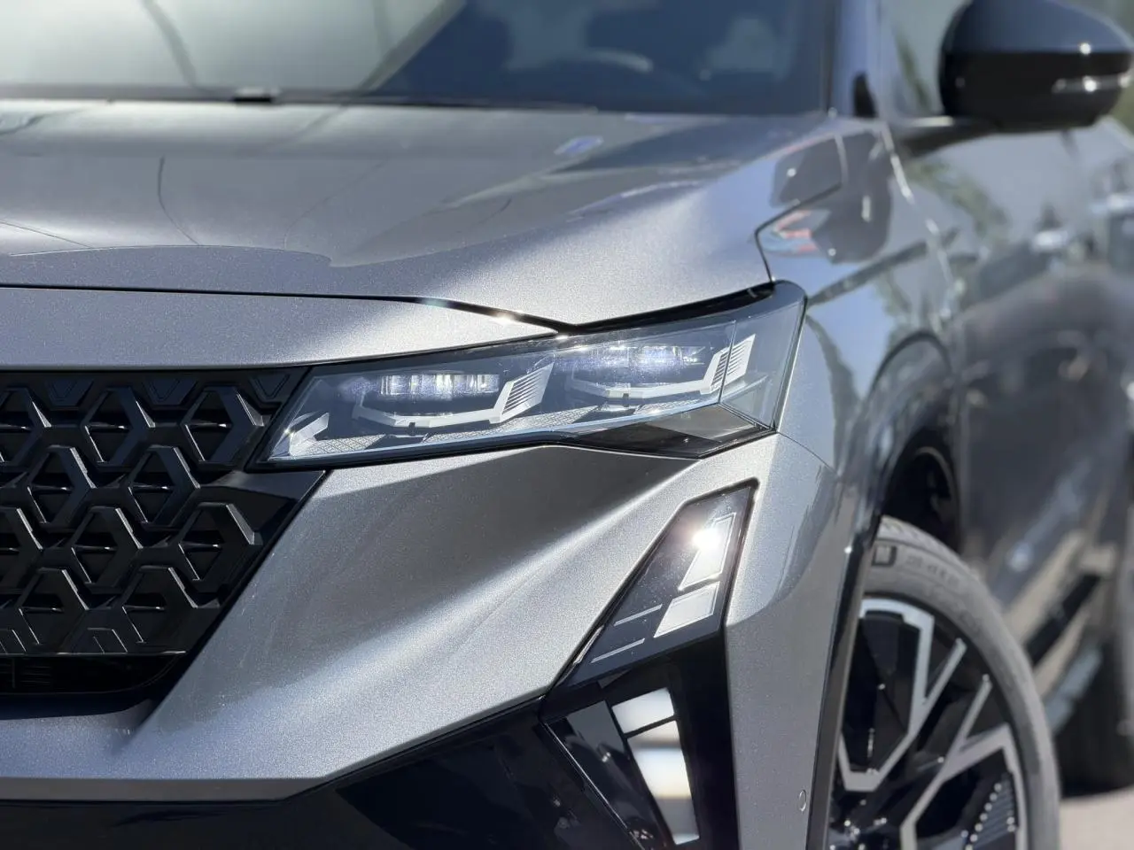 Gros plan sur l'avant droit gris schiste du Renault Austral 2026, mettant en valeur le phare LED et la calandre noire géométrique.