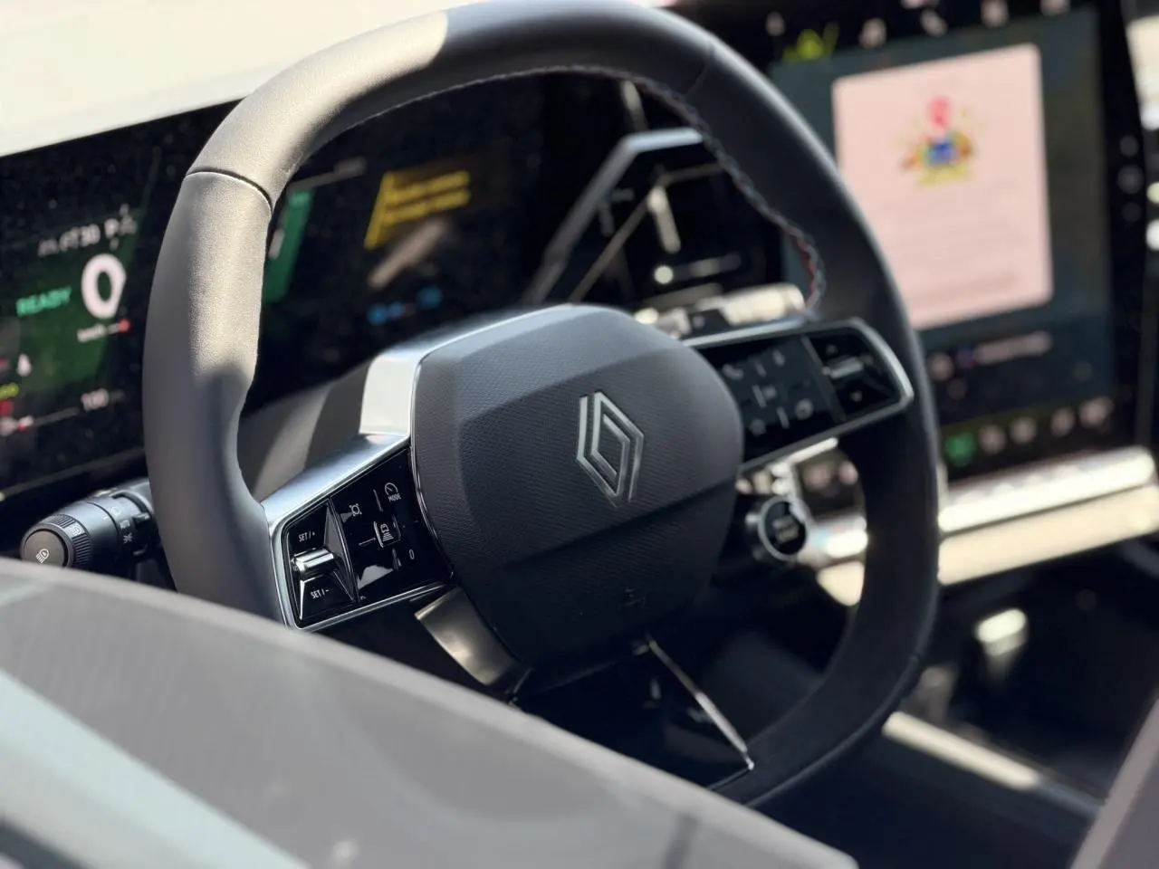 Vue rapprochée du volant noir au design moderne avec logo Renault, écran numérique et commandes intégrées visibles.