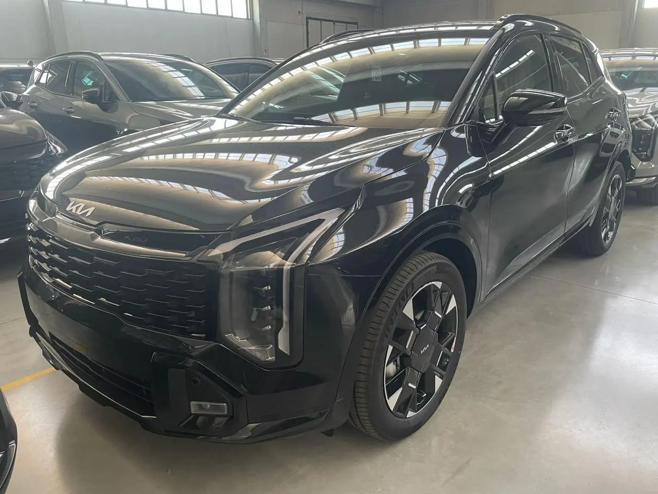 KIA SPORTAGE hybride noir 2026 vu en 3/4 avant droit avec calandre large et jantes noires distinctives.