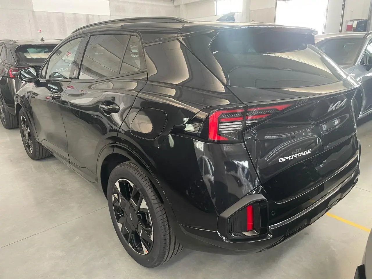 Vue 3/4 arrière droite du KIA Sportage hybride noir 2026 avec feux arrière LED et jantes noires distinctives GT-Line.