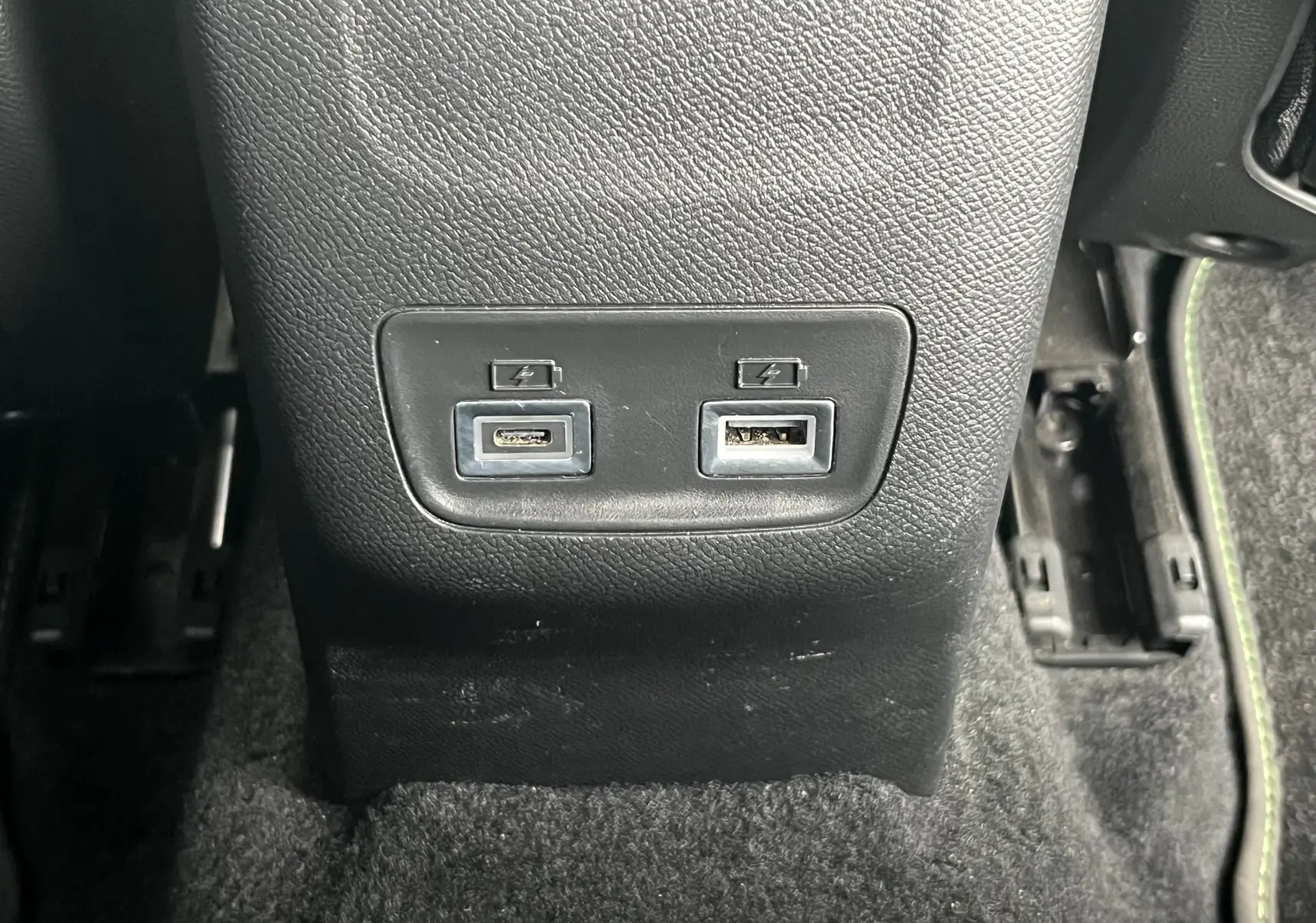 Prise USB et USB-C noires sur la console centrale arrière du Peugeot 2008 GT 2024, avec moquette foncée et surpiqûres vertes.