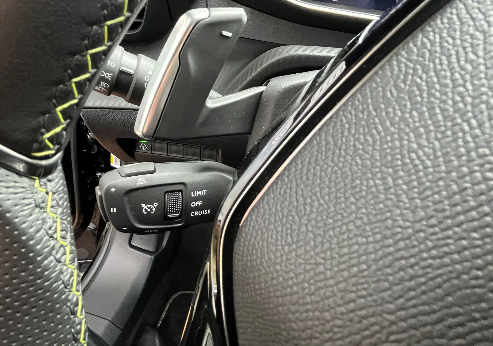 Gros plan sur la commande de régulateur de vitesse à gauche du volant noir avec surpiqûres jaunes du Peugeot 2008 GT 2024.