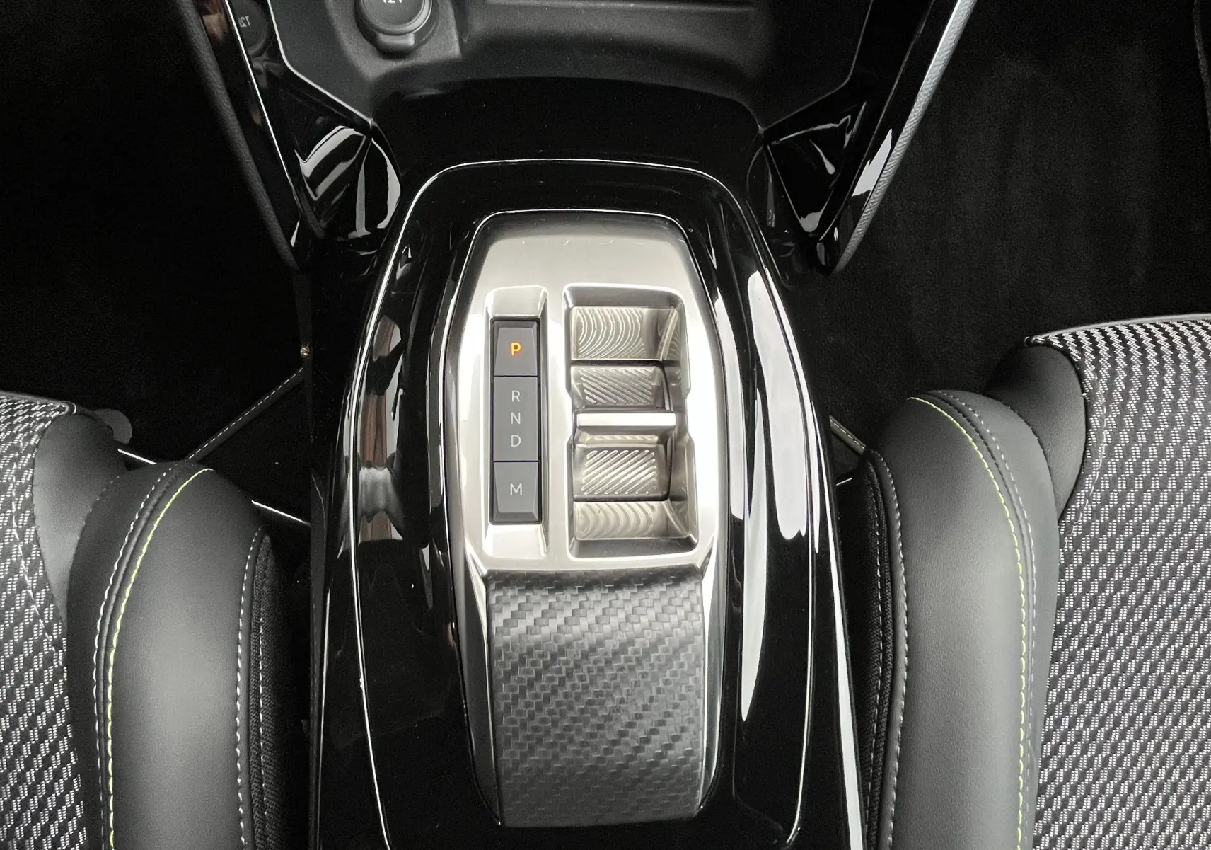 Vue plongeante sur la console centrale noire brillante du Peugeot 2008 2024 avec sélecteur de boîte auto et sièges tissu noir à surpiqûres vertes.