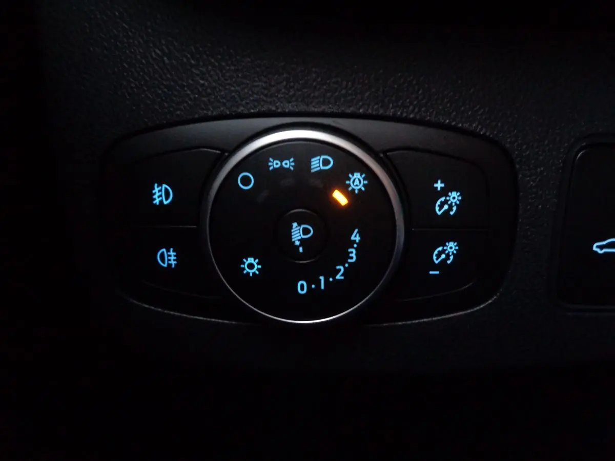 Gros plan sur le bouton de réglage des phares avec éclairage bleu et orange dans le Ford Puma noir Agate 2022.