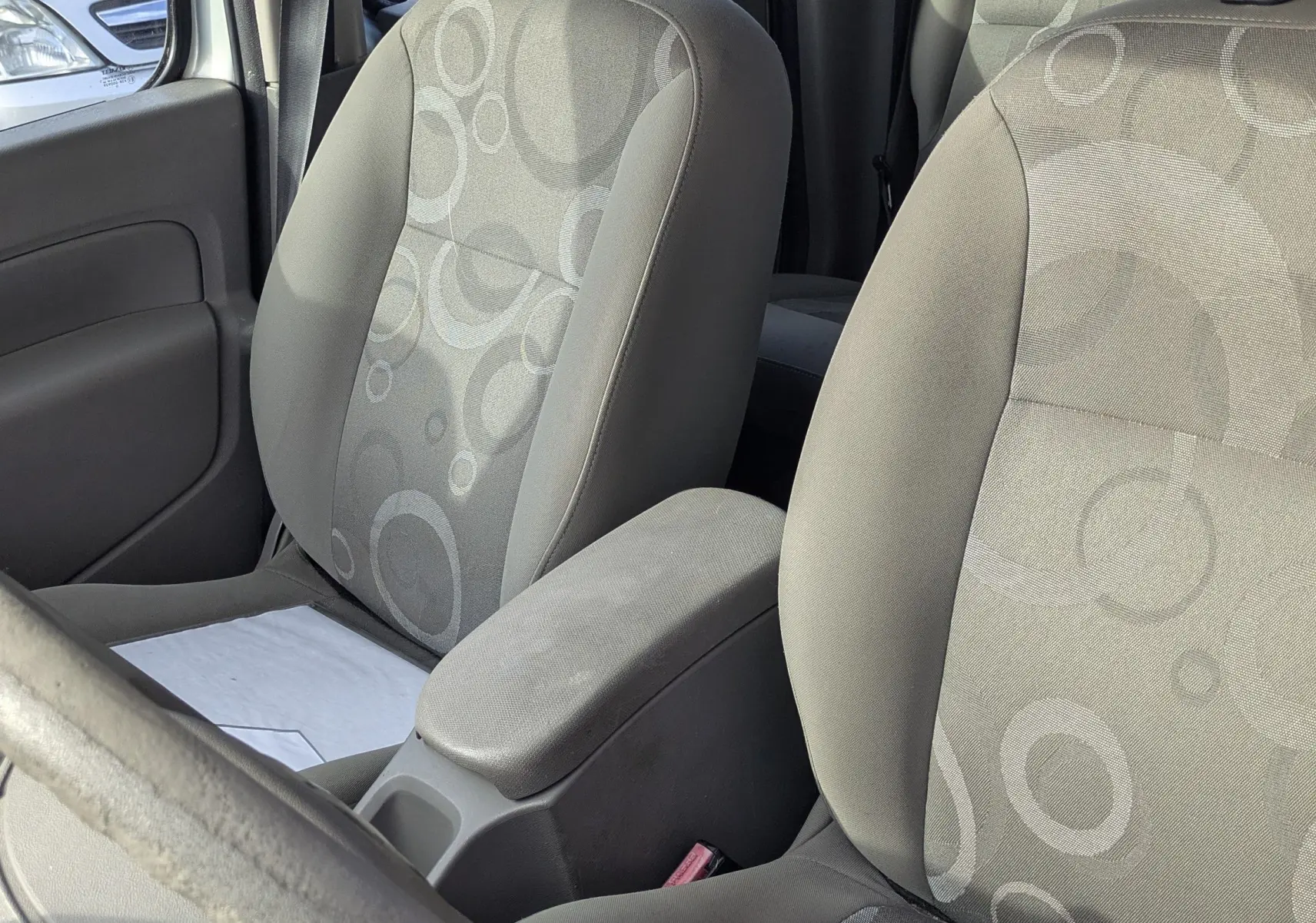 Vue intérieure des sièges avant gris à motifs ronds du Renault Kangoo II bleu ciel, avec accoudoir central visible.