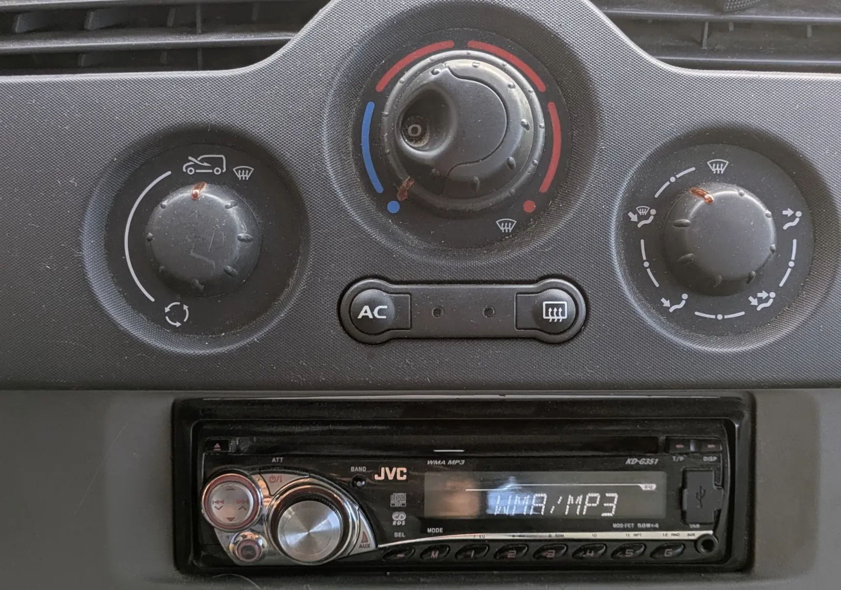 Gros plan sur la console centrale du Renault Kangoo II 2010 avec commandes de climatisation manuelle et autoradio JVC.
