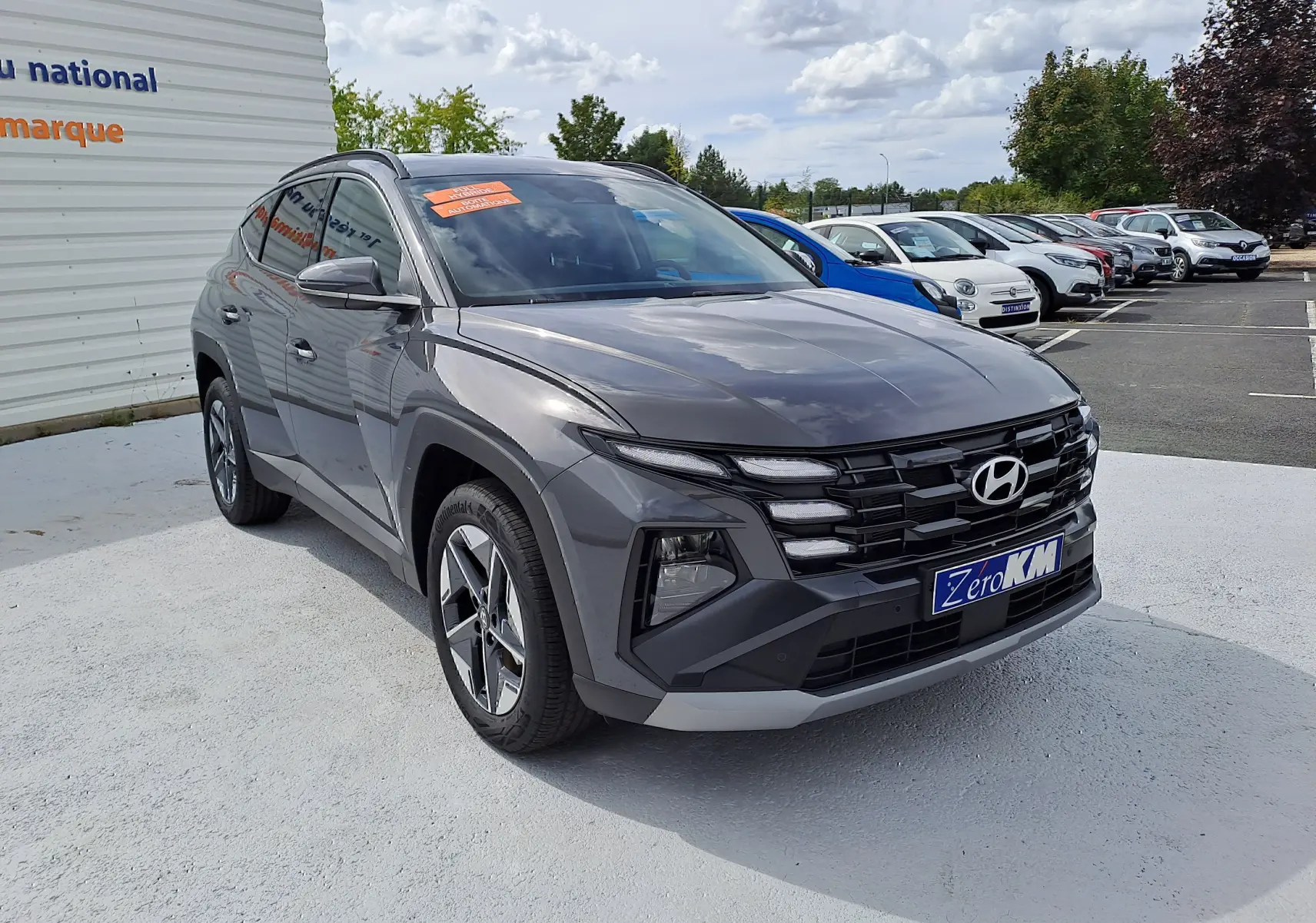 Vue 3/4 avant d'un Hyundai Tucson 2025 gris Ecotronic avec calandre noire et jantes alliage bicolores.