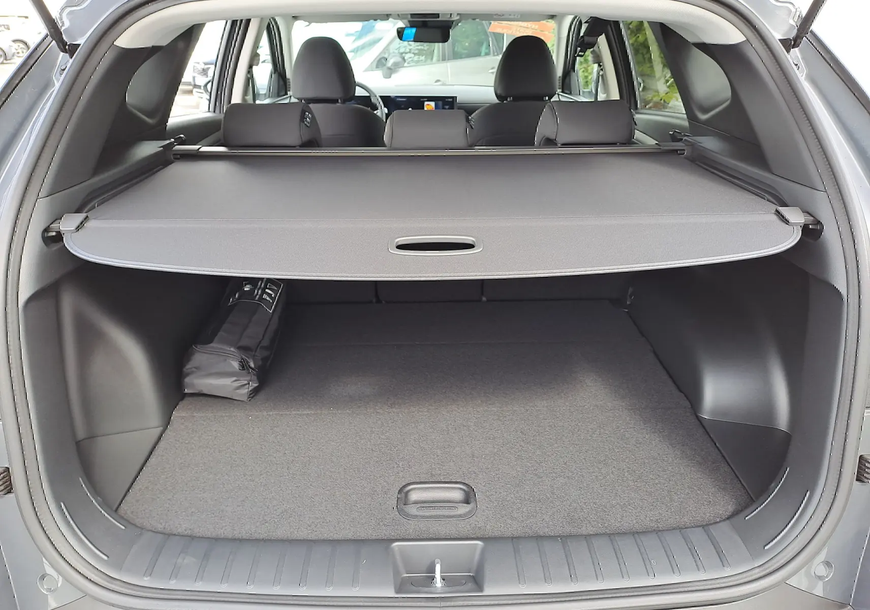 Coffre ouvert d'un Hyundai Tucson 2025 gris Ecotronic, avec cache-bagages déployé et intérieur noir visible.