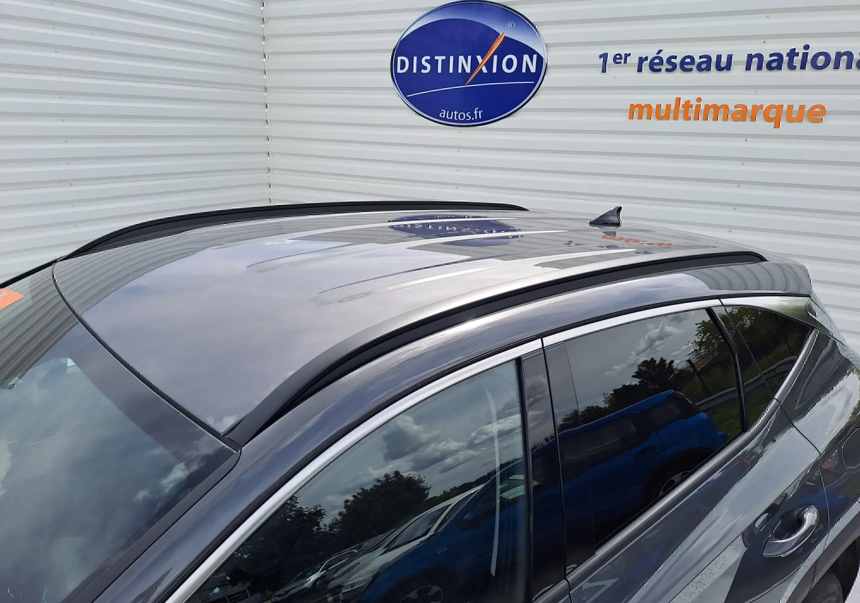 Vue latérale droite du Hyundai Tucson 2025 gris Ecotronic avec toit panoramique et vitres teintées, reflet de voitures environnantes visible.