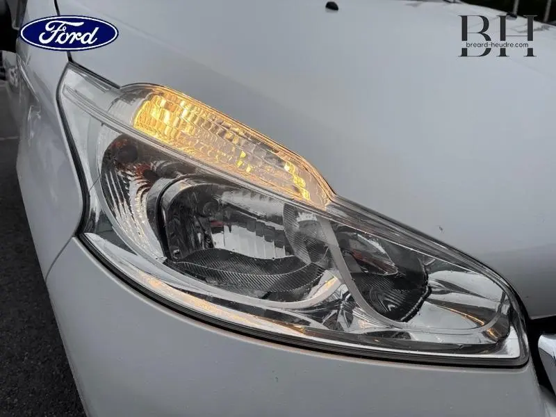 Gros plan sur le phare avant droit blanc Banquise d'une Peugeot 208 1.4 HDi FAP Access 2013 avec clignotant allumé.