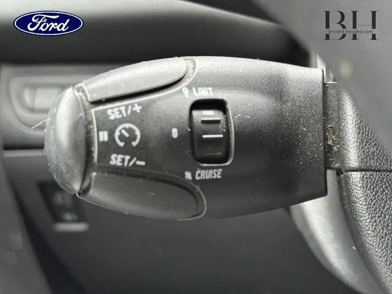 Levier de commande du régulateur de vitesse sur le volant d'une Peugeot 208 diesel blanc Banquise, vue rapprochée côté gauche.