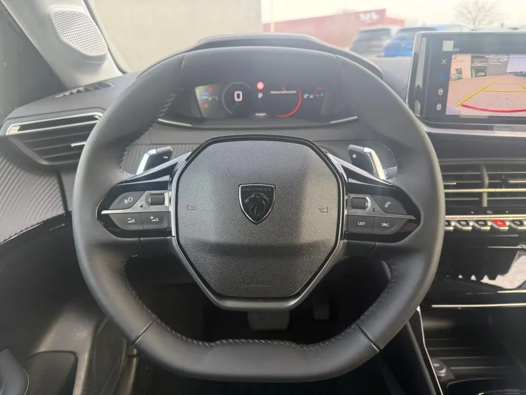 Vue intérieure centrée sur le volant noir de la Peugeot 208 Hybrid 110 e-DCS6 Allure avec tableau de bord numérique et écran tactile.