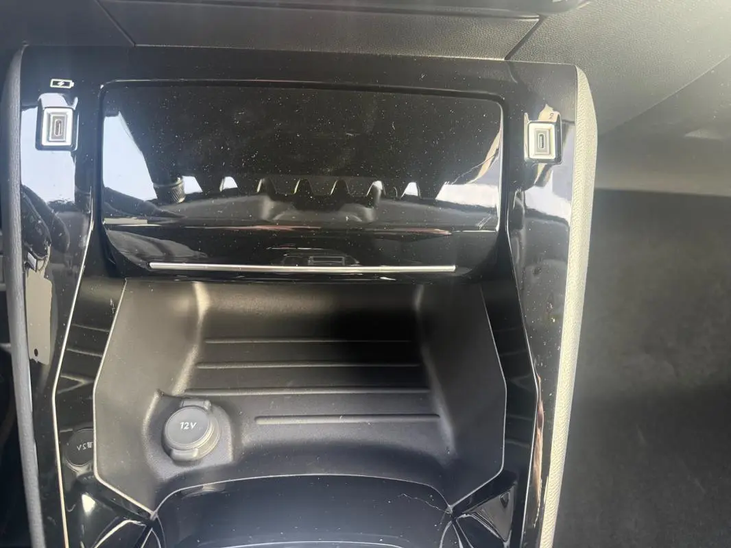 Gros plan sur la console centrale noire brillante du Peugeot 208 Hybrid 110, avec prise 12V visible en bas.